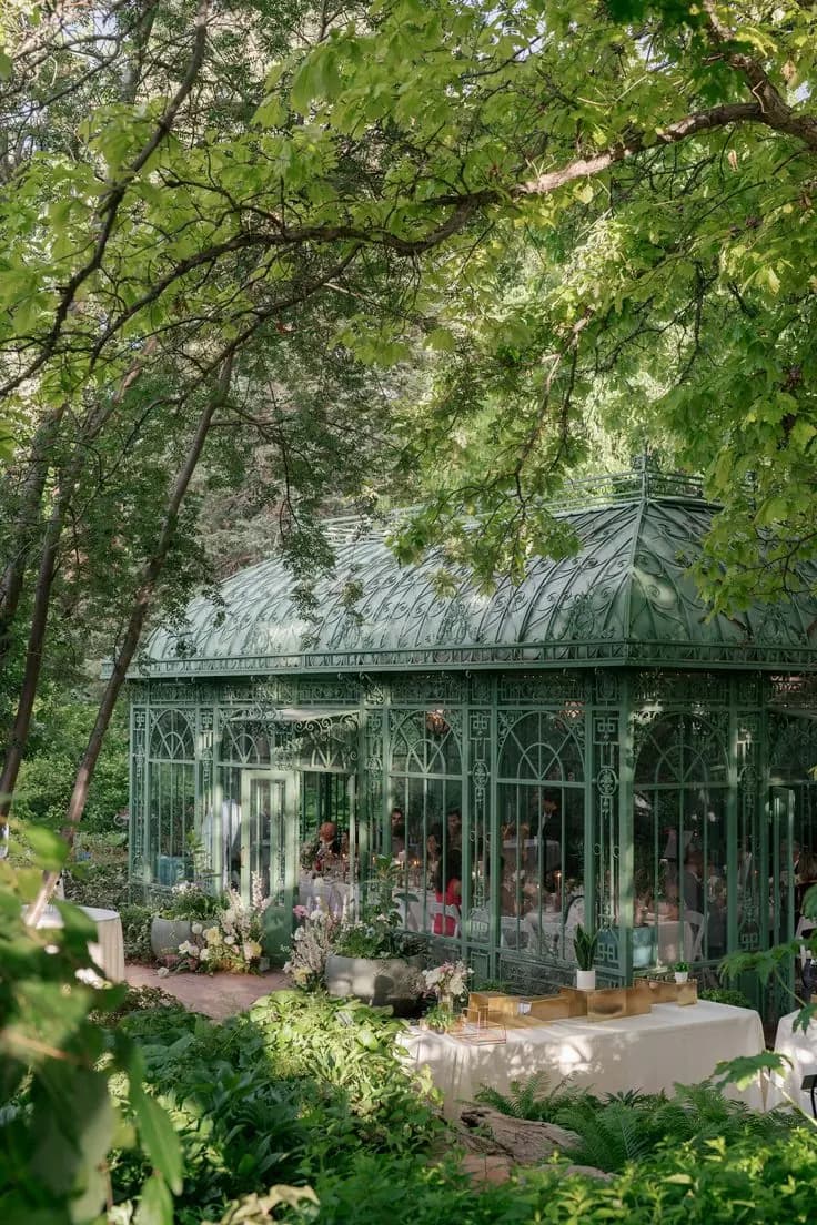 Wedding guests dining at round tables inside a Victorian glass conservatory surrounded by gardens